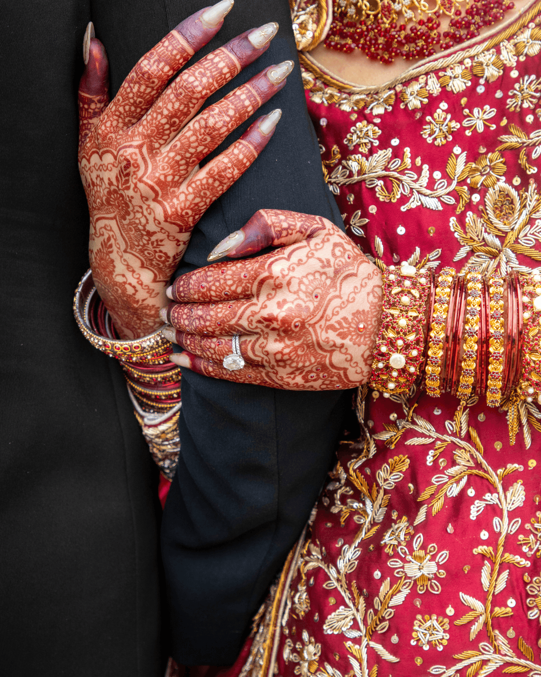 Henna-covered hands with long nails resting on a groom's arm
