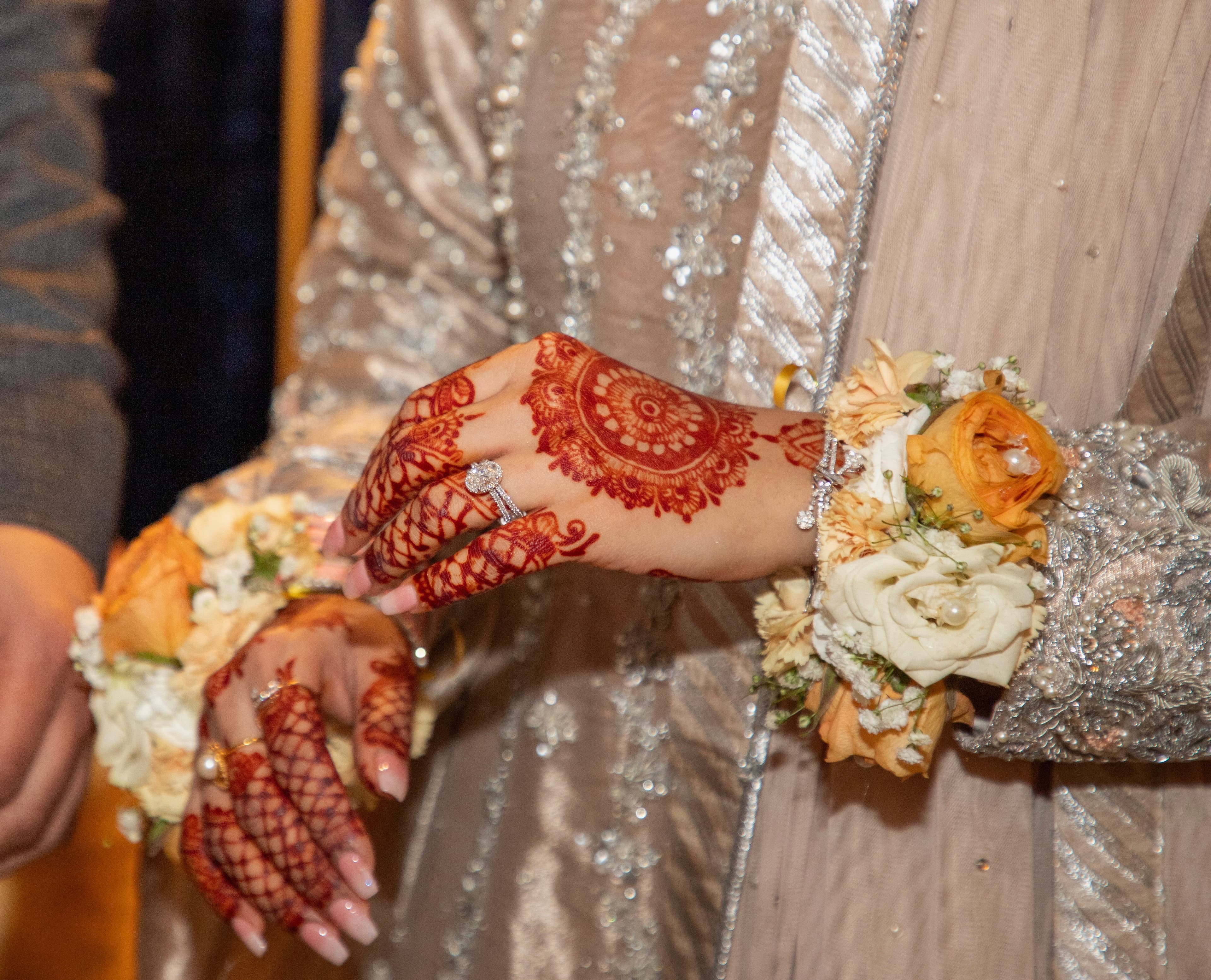 Close-up of henna-covered hands with rings and floral bracelets