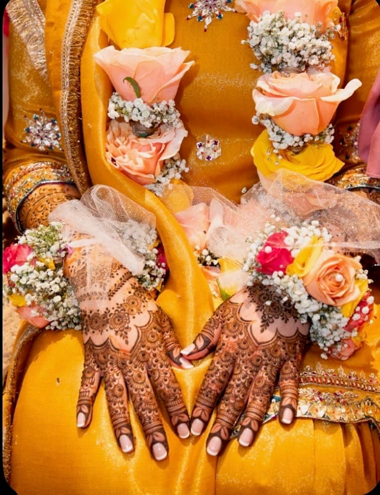 Henna-covered hands resting on a bright yellow mehndi outfit