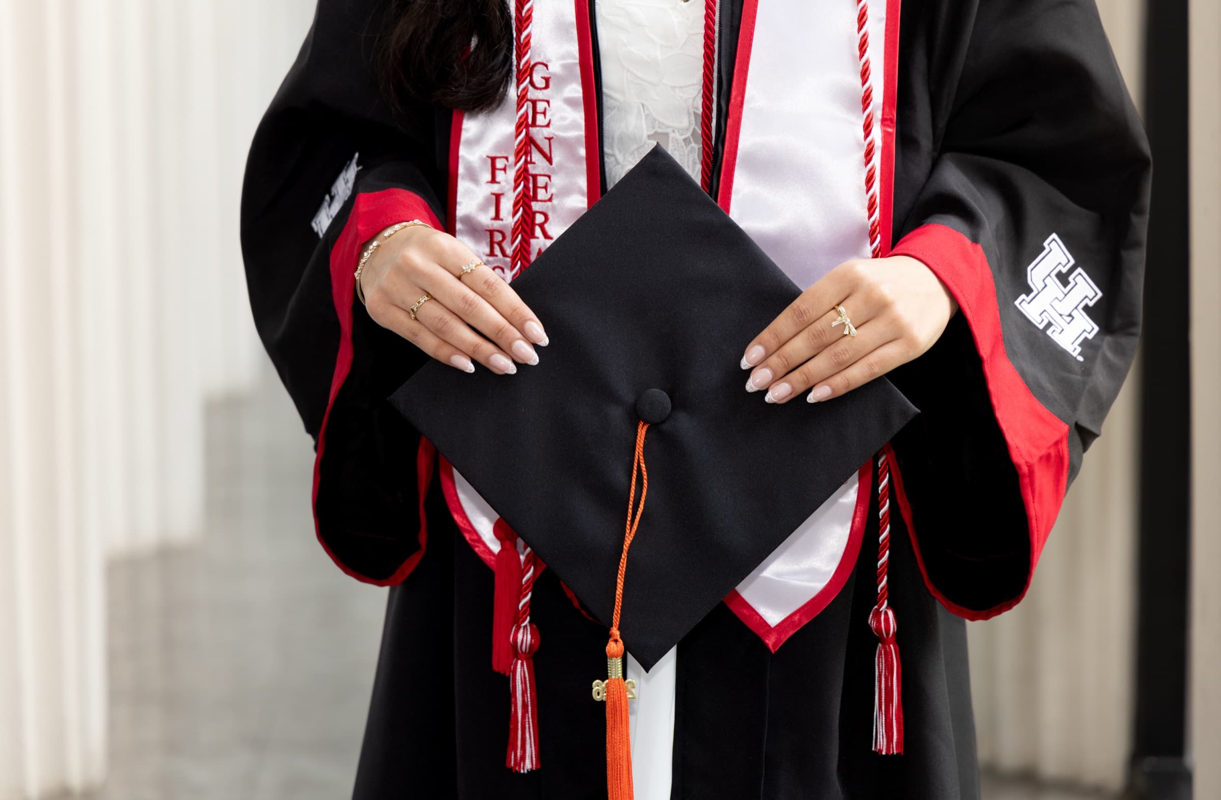 Close-up of a graduate's hands holding a cap, wearing University of Houston honor cords