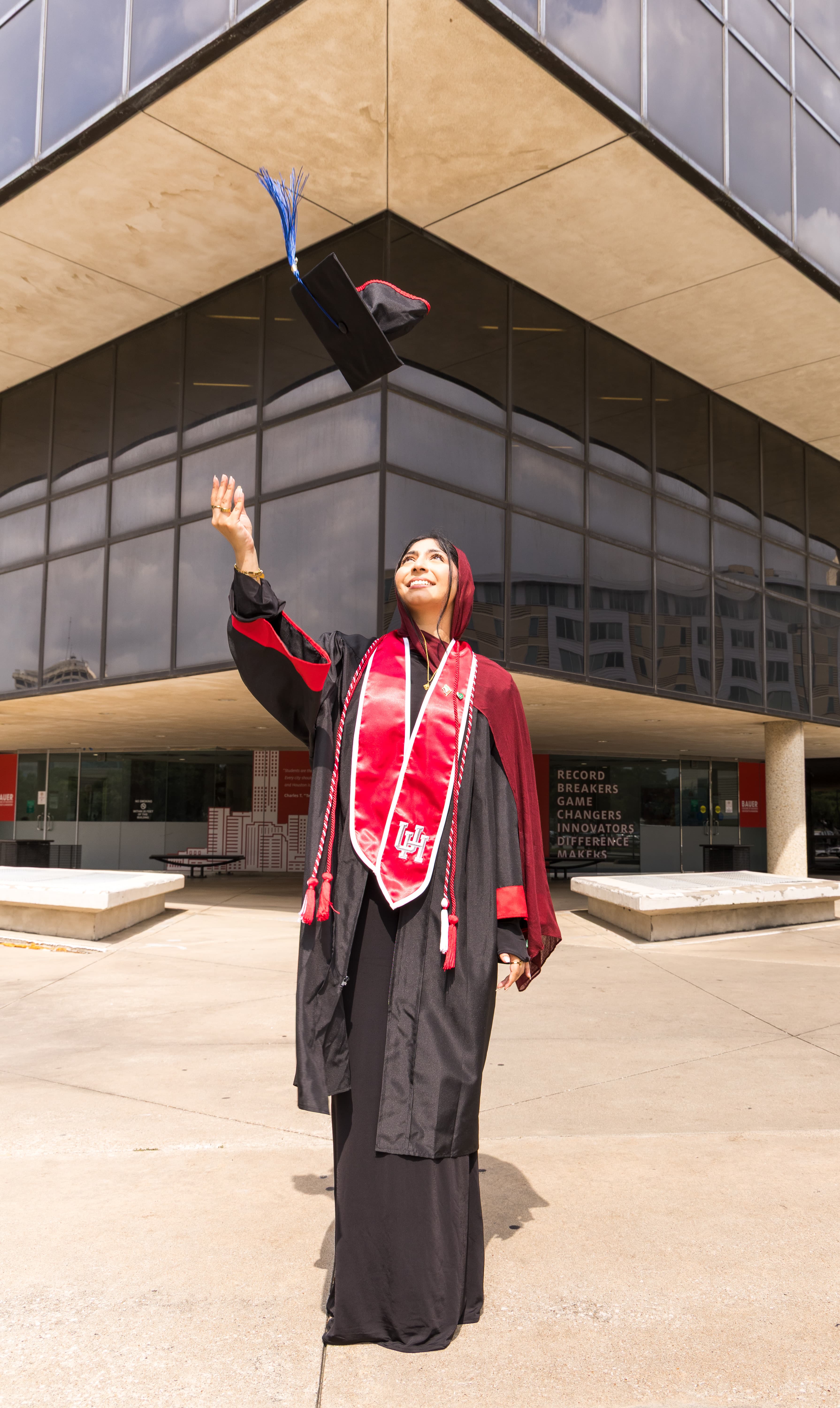 Graduate tossing her cap into the air in front of a modern building