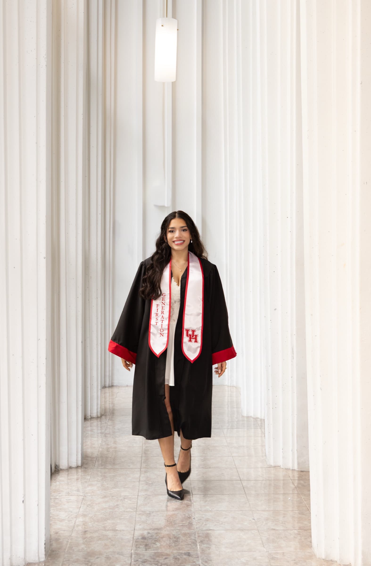 Graduate walking between white columns wearing a First Generation stole