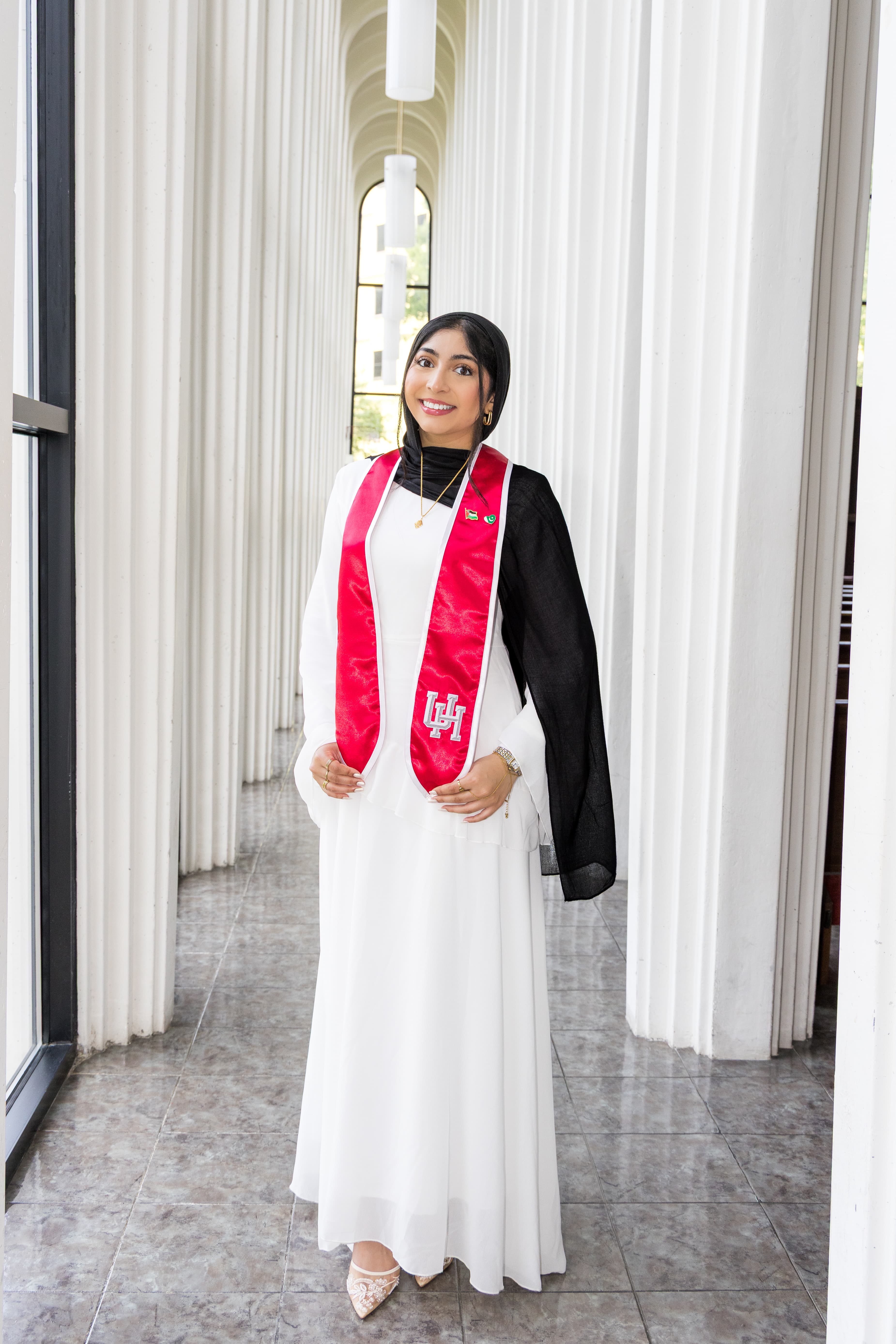 Graduate in a white dress and red stole standing among white columns