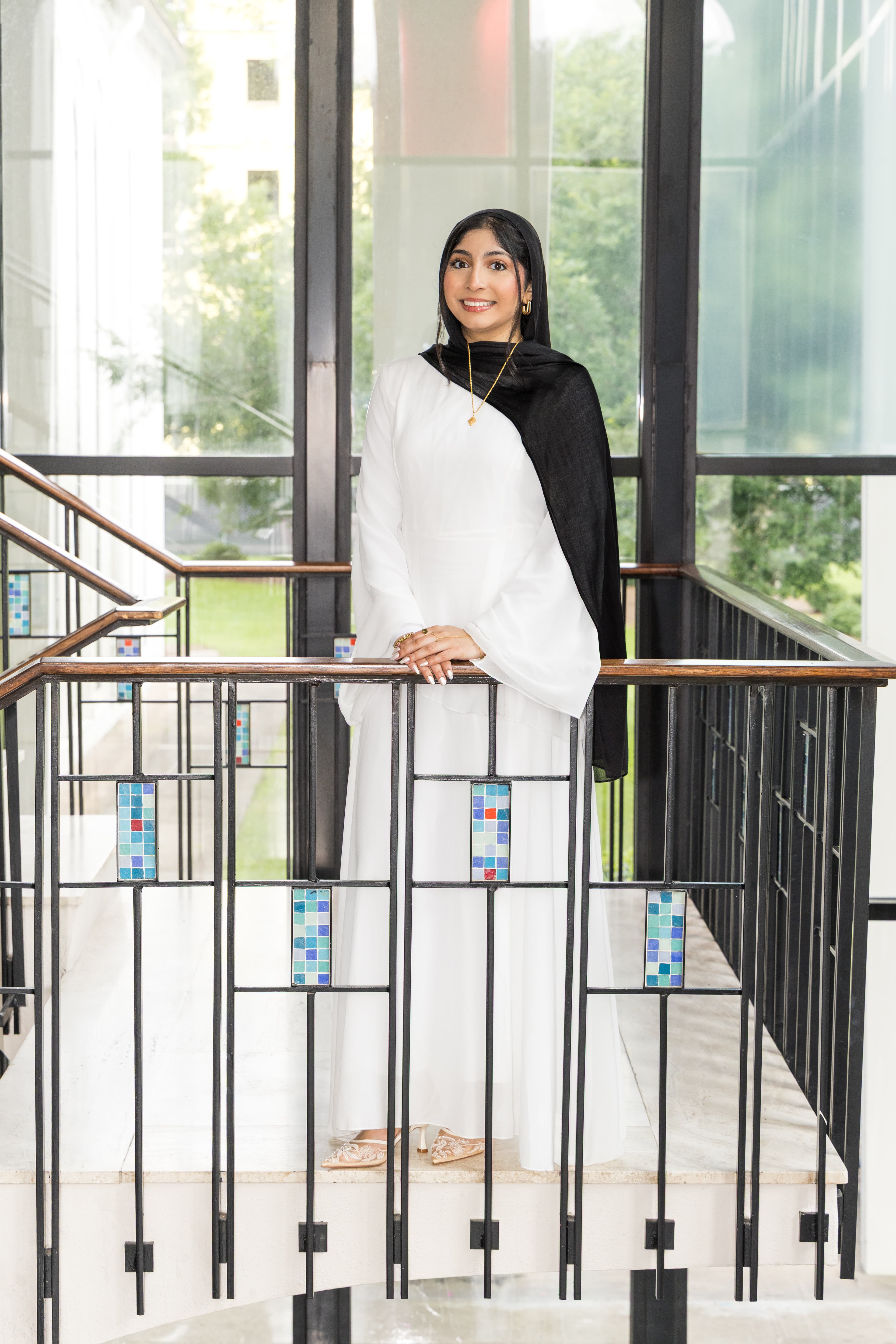 Graduate posing on a staircase in front of large glass windows