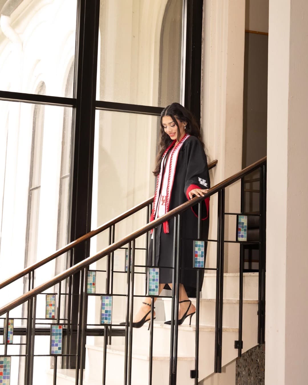 Graduate descending a staircase wearing a graduation gown with red stole