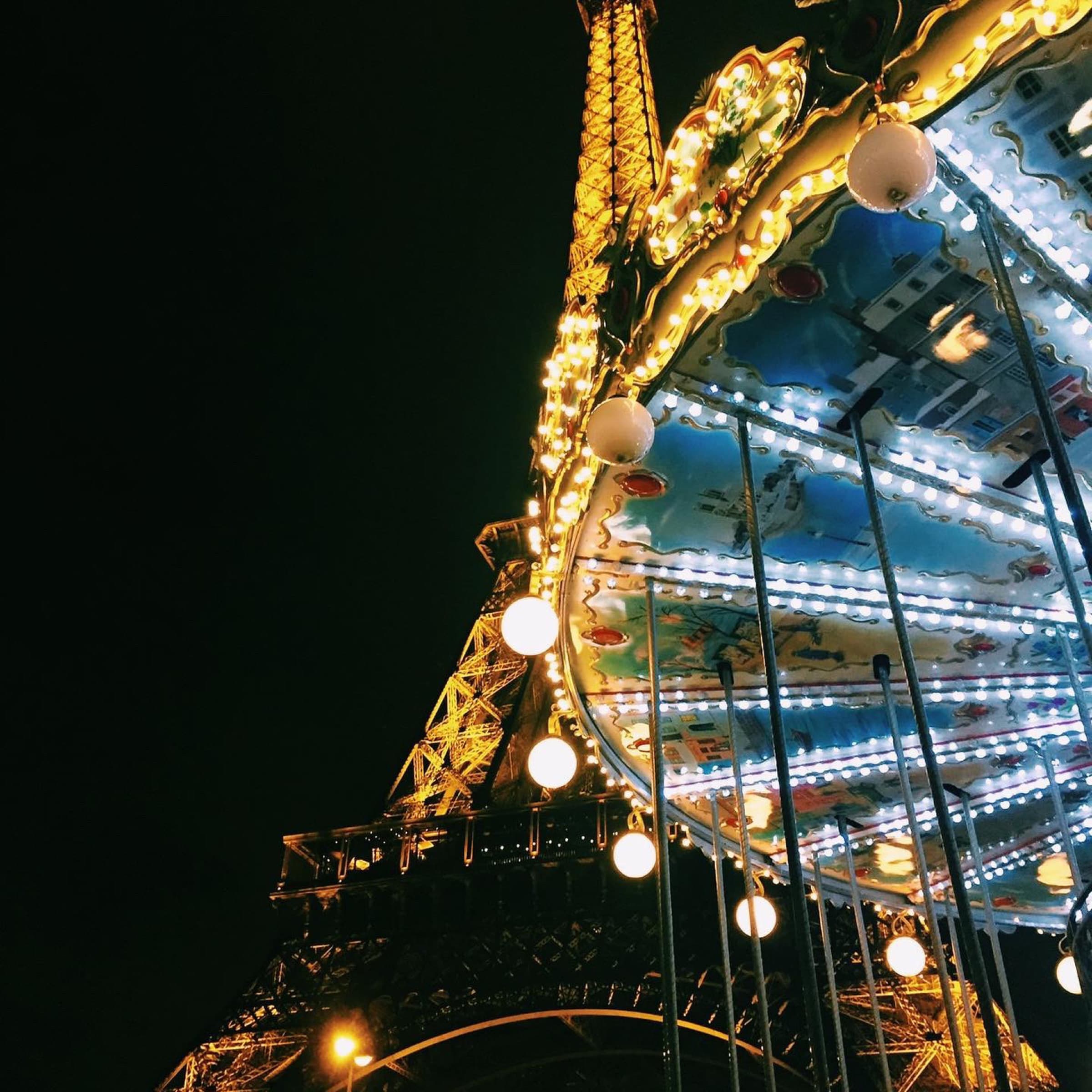 Eiffel Tower lit gold beside a carousel at night