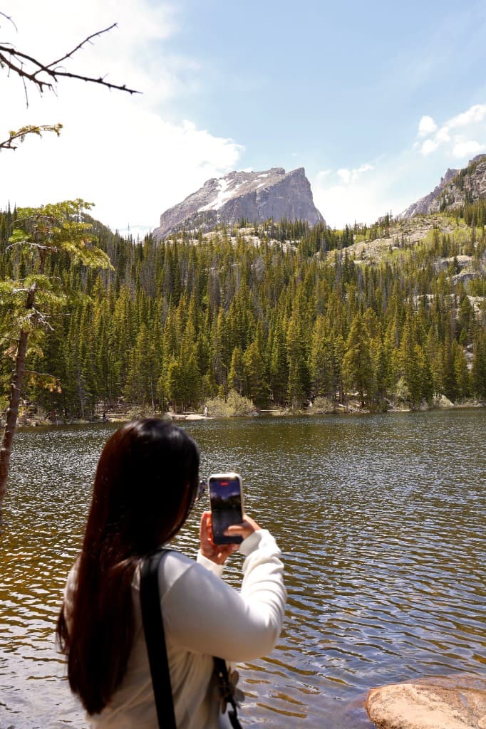 Woman photographing a mountain lake surrounded by pine forest