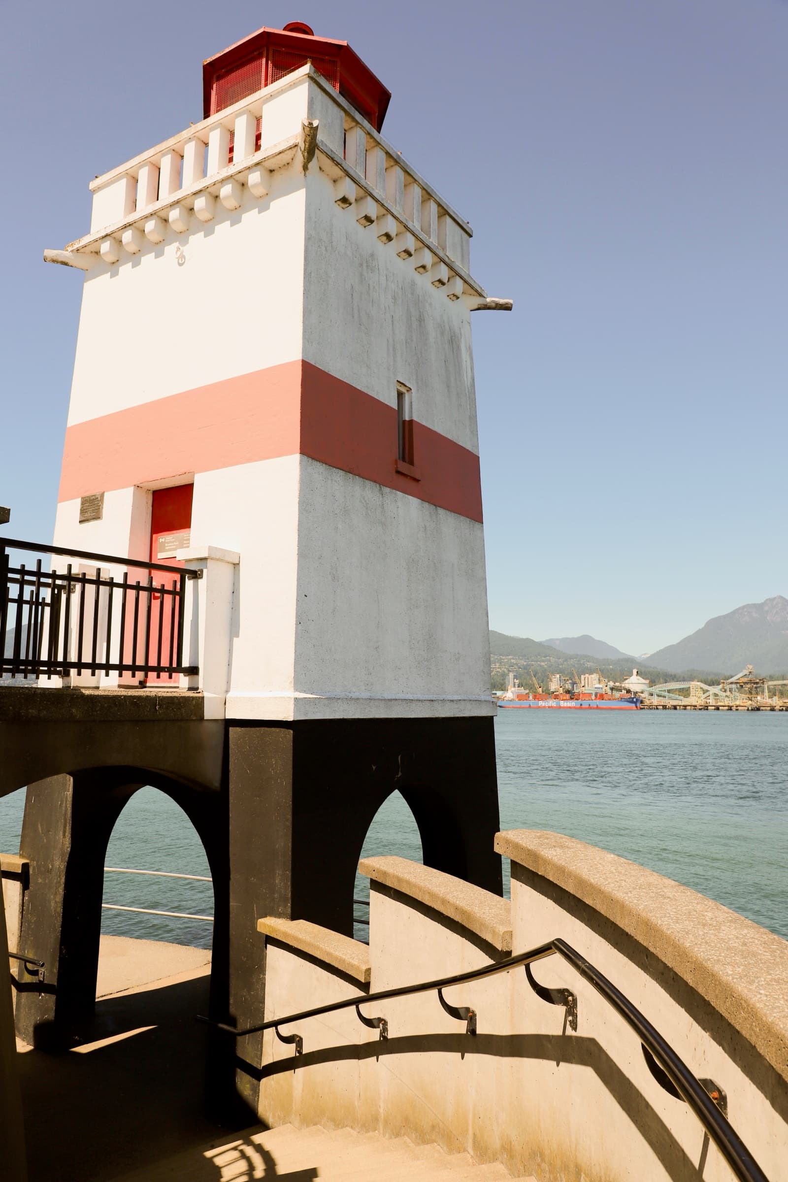 Red and white lighthouse on a pier overlooking the harbor and mountains