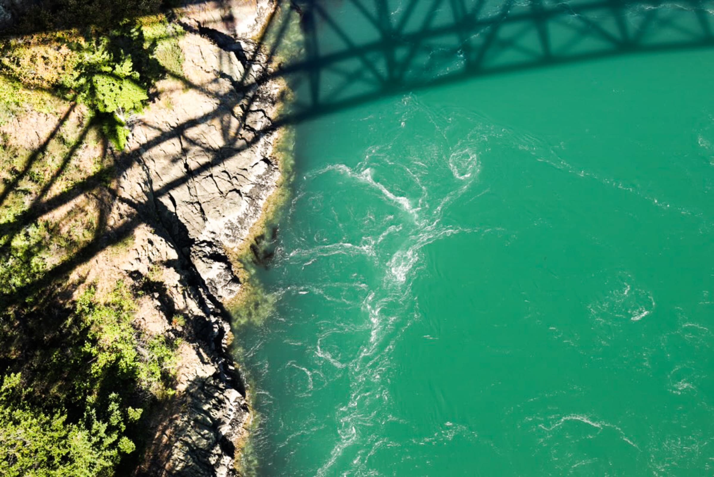 Aerial view of a turquoise river and forested shoreline beneath a bridge