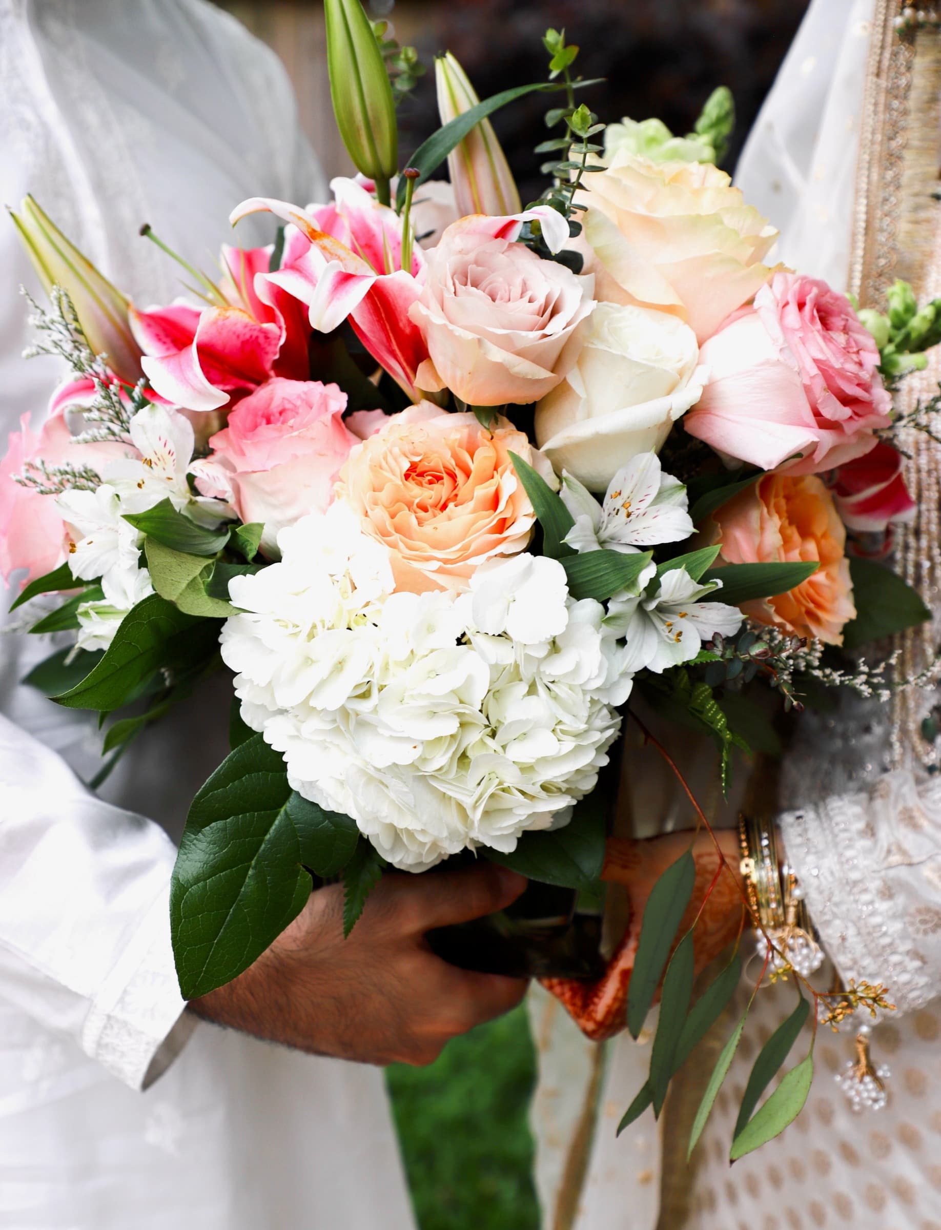 Close-up of a bridal bouquet with pink roses, lilies, and hydrangeas