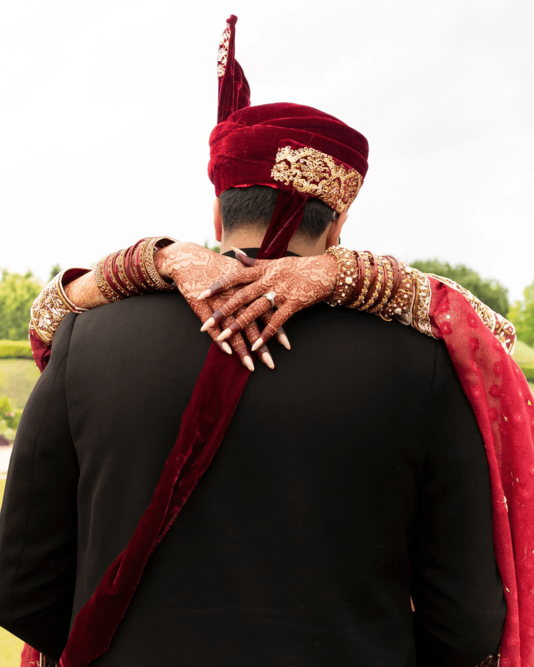 Bride resting her hands on groom's shoulders from behind, wearing a maroon dupatta