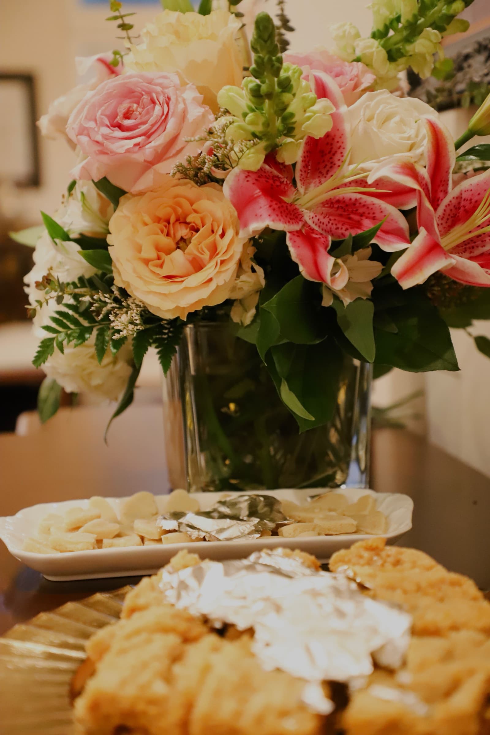 Floral centerpiece with lilies and roses beside a dessert table