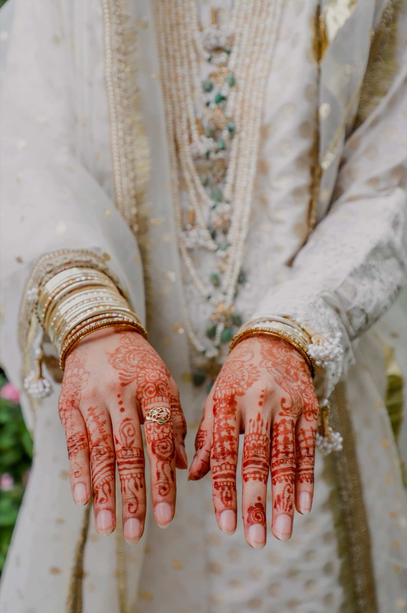 Bride's henna-covered hands adorned with bangles and layered pearls