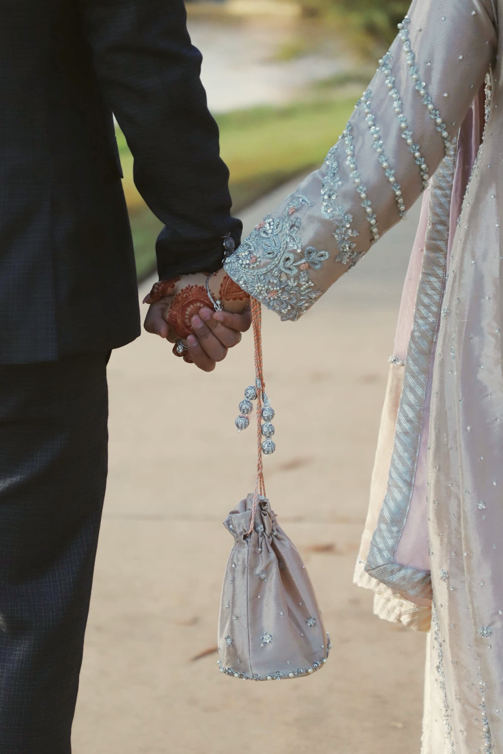 Bride and groom holding hands, her henna-adorned wrist holding an embroidered potli bag