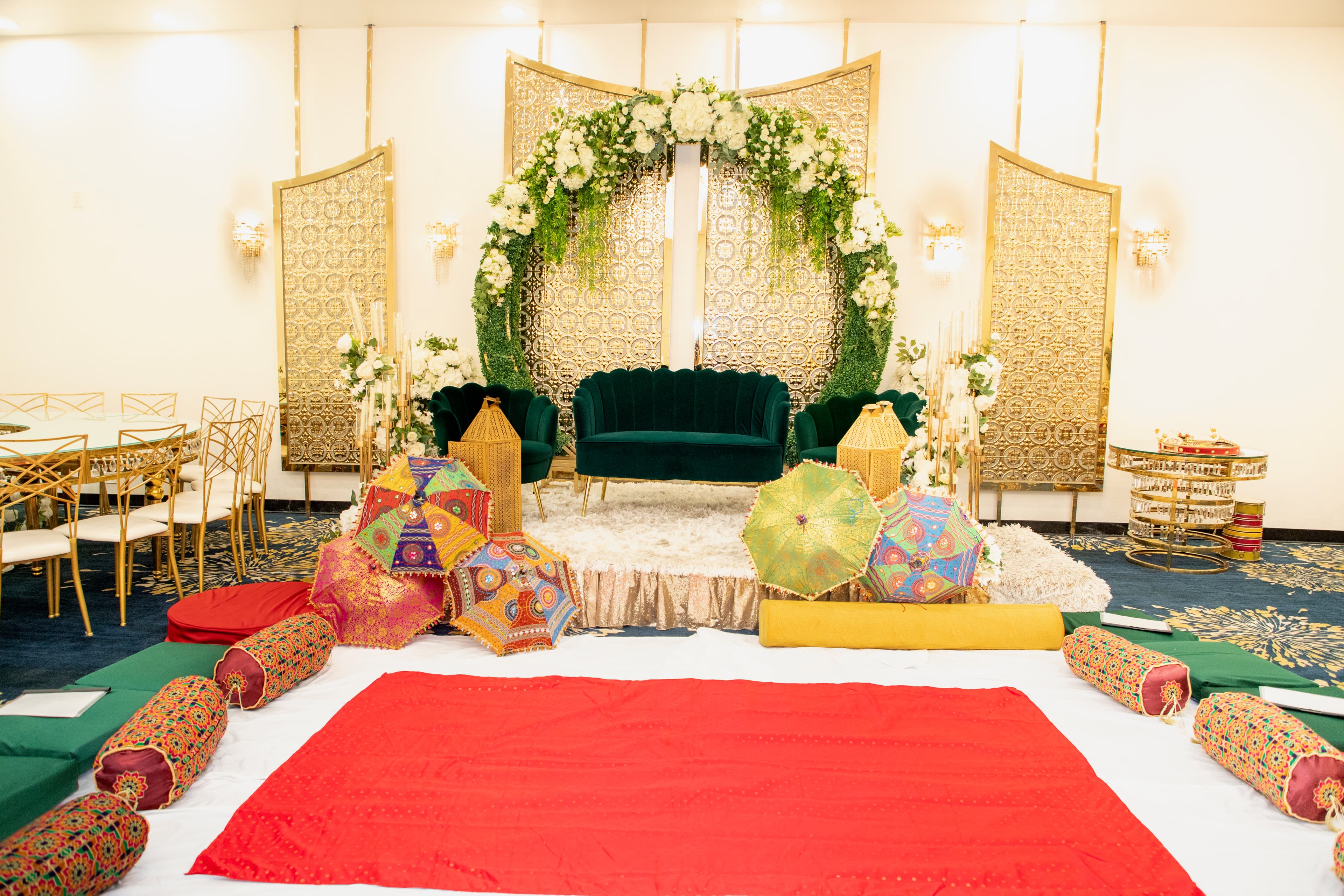 Mehndi stage setup with green velvet sofas, gold panels, and floral arch