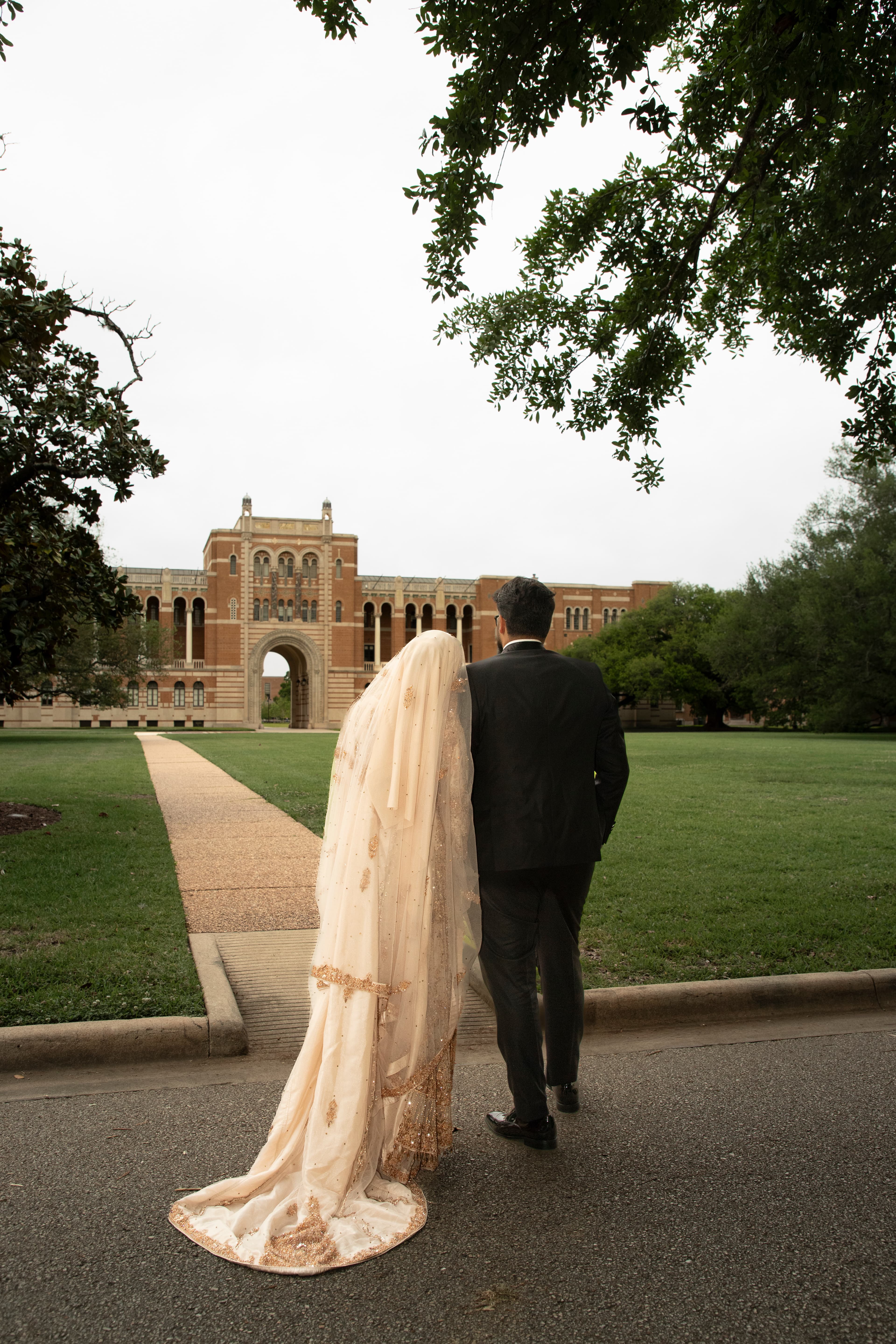 Bride and groom walking hand in hand toward a university archway
